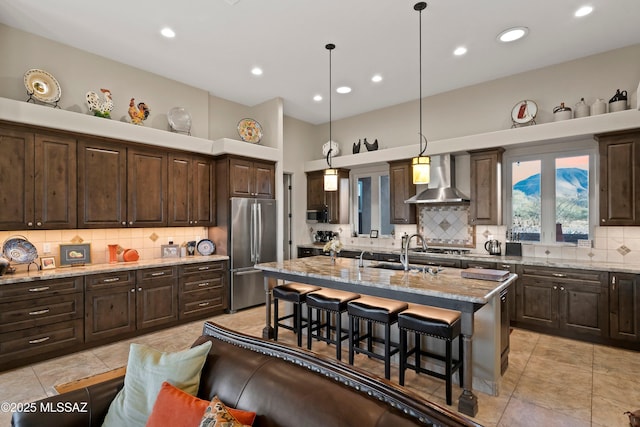 kitchen featuring dark brown cabinets, wall chimney range hood, stainless steel fridge, and a breakfast bar