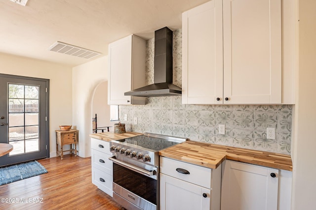 kitchen featuring wall chimney exhaust hood, butcher block counters, stainless steel stove, and white cabinets