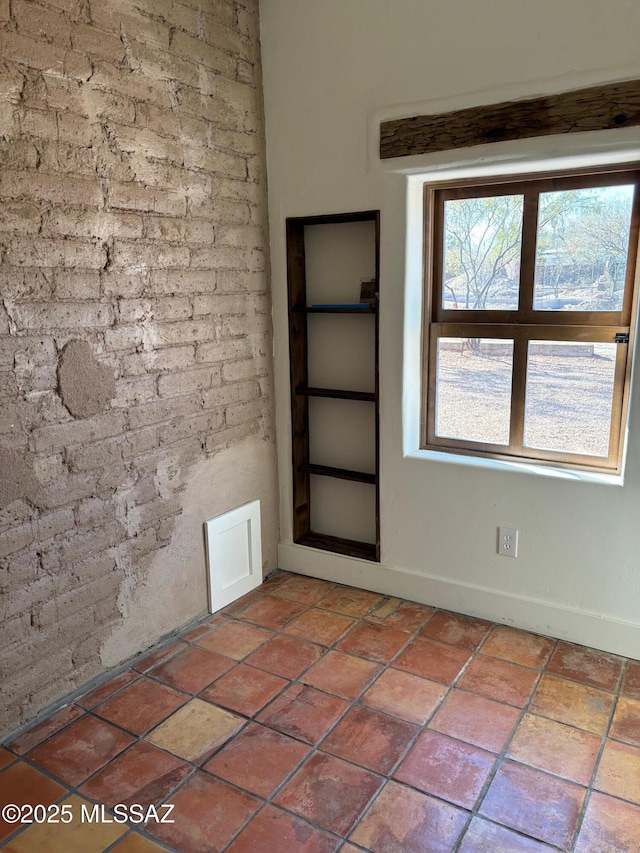 tiled spare room featuring brick wall