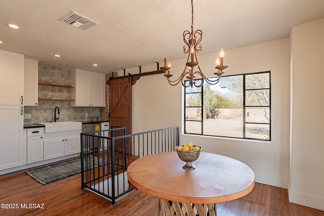 dining room with hardwood / wood-style flooring, a barn door, sink, and a notable chandelier