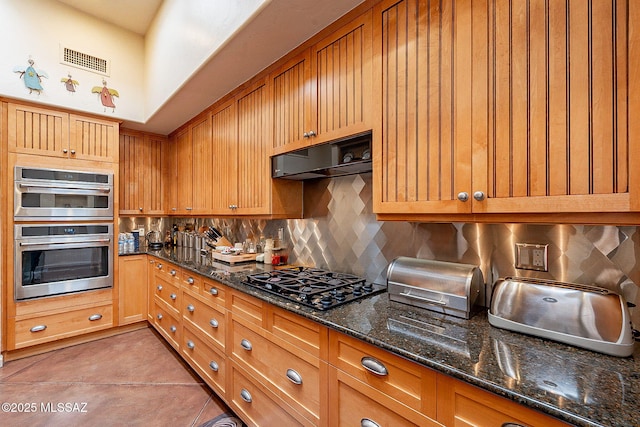 kitchen featuring double oven, exhaust hood, light tile patterned floors, black gas cooktop, and dark stone countertops