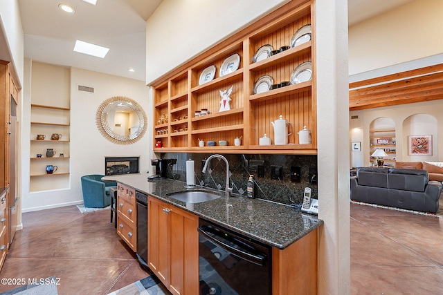 kitchen with dishwasher, a skylight, dark stone counters, and sink