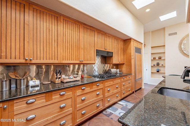 kitchen featuring tasteful backsplash, lofted ceiling with skylight, stainless steel gas cooktop, sink, and dark stone countertops