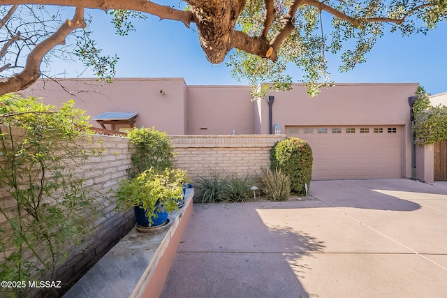 exterior space with concrete driveway, an attached garage, fence, and stucco siding