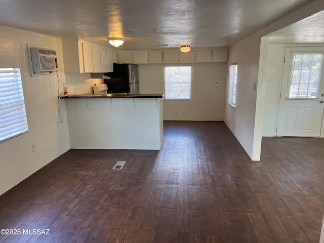 kitchen featuring an AC wall unit, kitchen peninsula, stainless steel fridge, and dark hardwood / wood-style floors