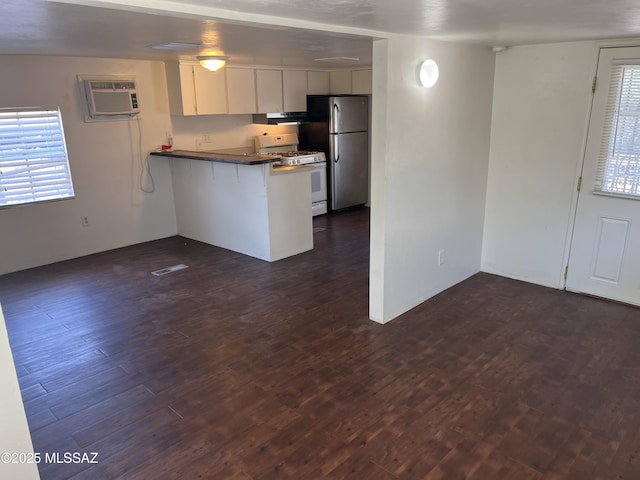 kitchen featuring kitchen peninsula, a wall mounted air conditioner, white gas range, dark hardwood / wood-style floors, and white cabinetry