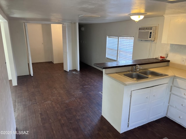 kitchen with sink, a wall mounted air conditioner, dark hardwood / wood-style floors, kitchen peninsula, and white cabinets