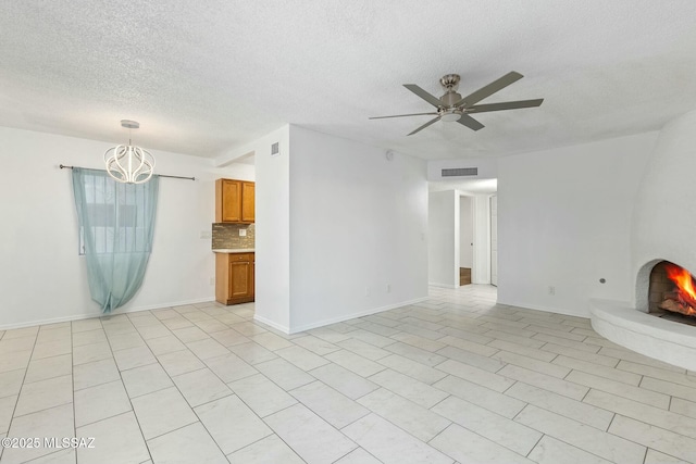 unfurnished living room with ceiling fan with notable chandelier, a textured ceiling, and a fireplace