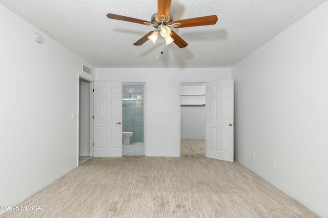 unfurnished bedroom featuring a walk in closet, ensuite bath, a closet, and a textured ceiling