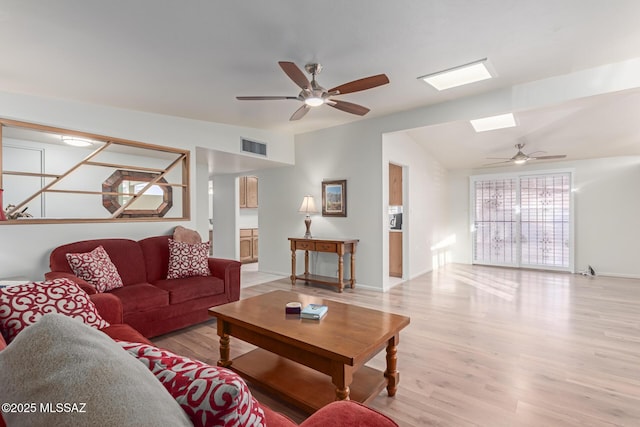 living room with light hardwood / wood-style flooring, ceiling fan, and vaulted ceiling with skylight