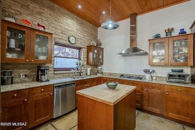 kitchen with a center island, sink, wall chimney exhaust hood, light stone countertops, and stainless steel appliances