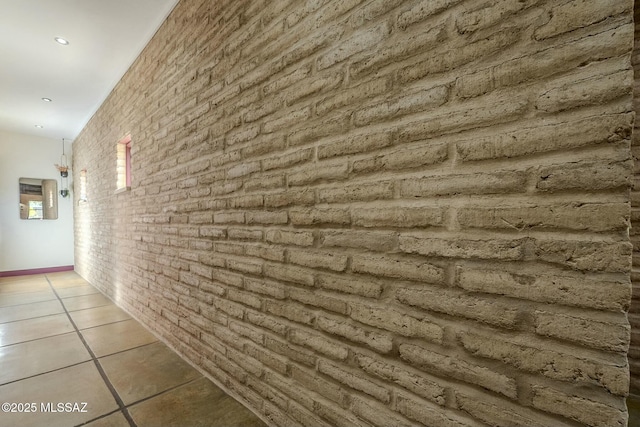 hall featuring light tile patterned flooring and brick wall