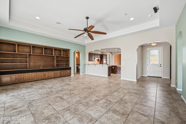 unfurnished living room with built in features, ceiling fan, and a tray ceiling