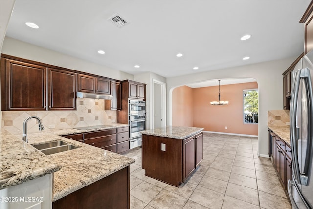 kitchen with a center island, pendant lighting, light stone counters, sink, and backsplash