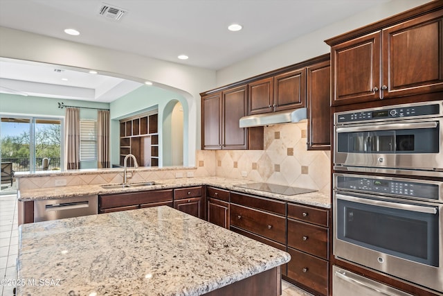 kitchen with sink, stainless steel appliances, light stone countertops, and decorative backsplash