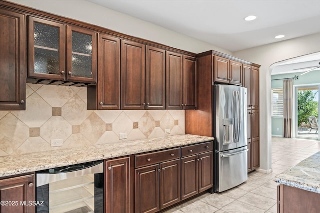 kitchen with light tile patterned floors, beverage cooler, backsplash, stainless steel fridge with ice dispenser, and light stone countertops