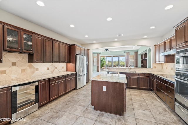 kitchen featuring beverage cooler, stainless steel fridge with ice dispenser, ceiling fan, a kitchen island, and tasteful backsplash