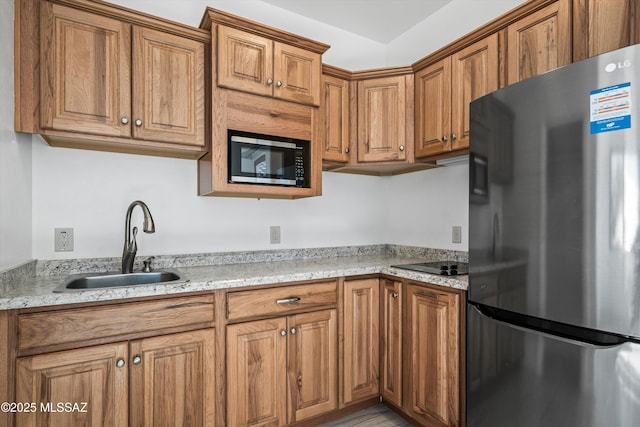 kitchen with stainless steel refrigerator, light stone countertops, black electric stovetop, and sink