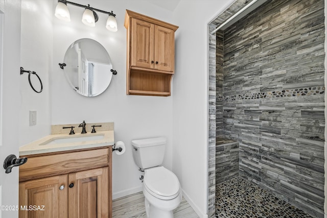 bathroom featuring toilet, a tile shower, and vanity