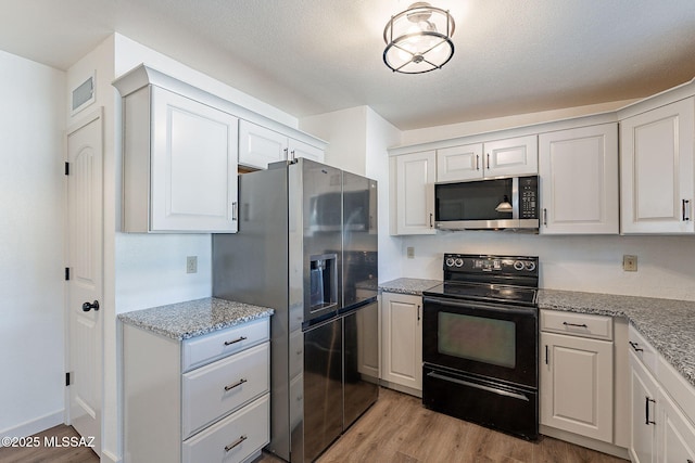 kitchen with white cabinetry, light stone counters, light hardwood / wood-style flooring, a textured ceiling, and appliances with stainless steel finishes