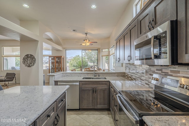 kitchen with sink, dark brown cabinets, stainless steel appliances, light stone countertops, and decorative backsplash