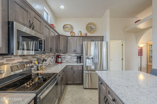 kitchen with stainless steel appliances, light stone countertops, dark brown cabinets, and backsplash