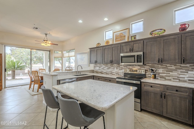 kitchen with appliances with stainless steel finishes, light stone countertops, sink, and a kitchen island