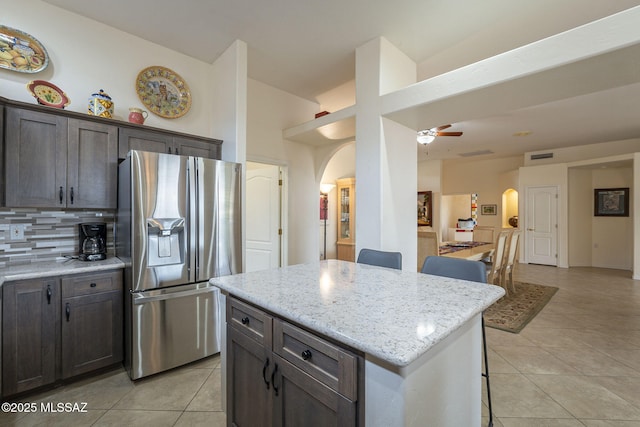 kitchen featuring stainless steel refrigerator with ice dispenser, light stone counters, a kitchen island, and light tile patterned floors