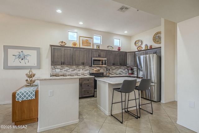 kitchen featuring dark brown cabinetry, tasteful backsplash, stainless steel appliances, and a center island