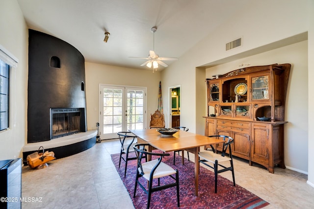 tiled dining room with lofted ceiling, a large fireplace, ceiling fan, and french doors