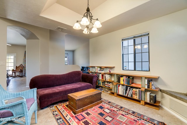 tiled living room featuring a raised ceiling and a chandelier