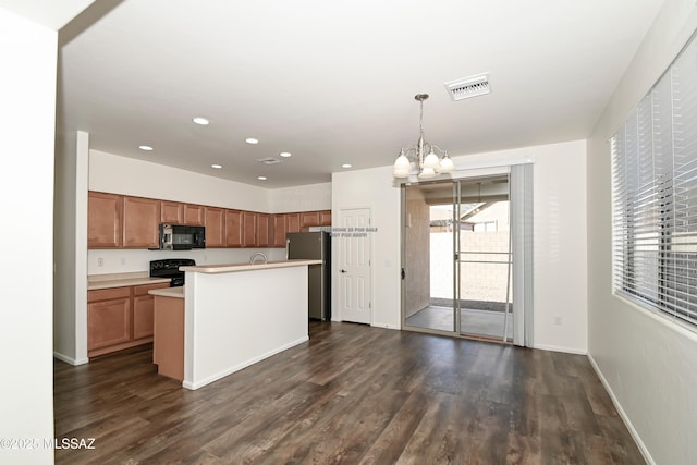 kitchen with dark wood-type flooring, a chandelier, pendant lighting, an island with sink, and black appliances