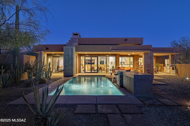 back house at dusk featuring a fenced in pool, a patio, exterior bar, and exterior kitchen