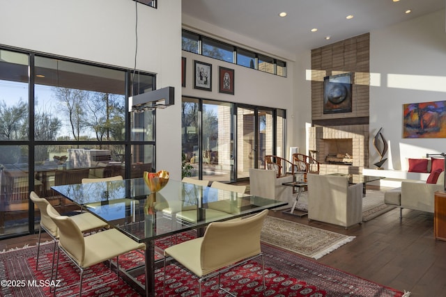 dining room featuring a towering ceiling, wood-type flooring, and a brick fireplace