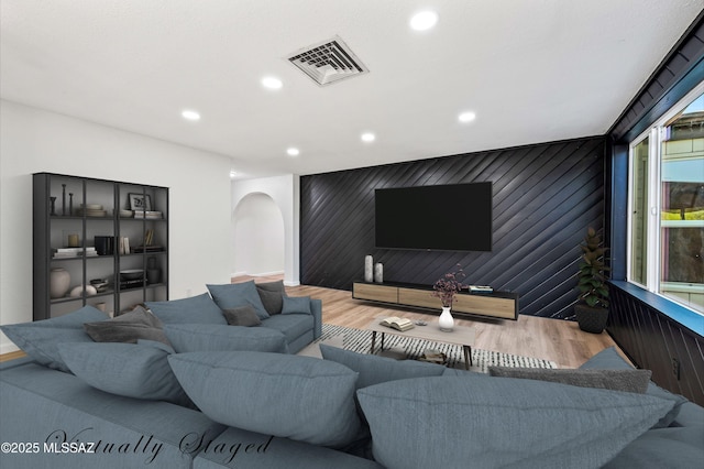 living room featuring wooden walls, visible vents, arched walkways, wood finished floors, and recessed lighting