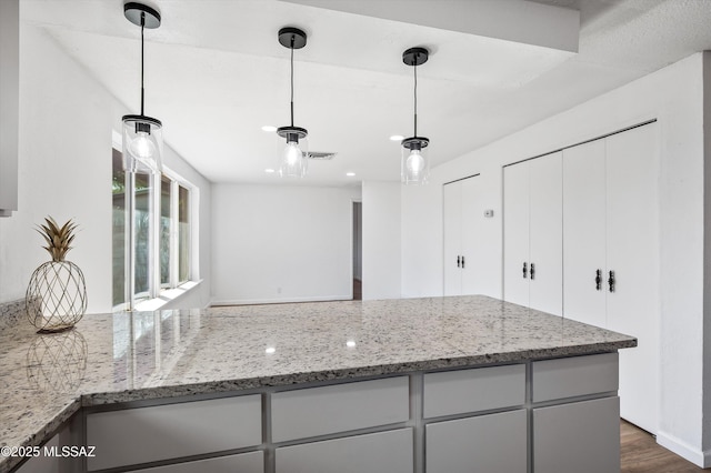 kitchen featuring visible vents, dark wood-style floors, light stone countertops, and pendant lighting