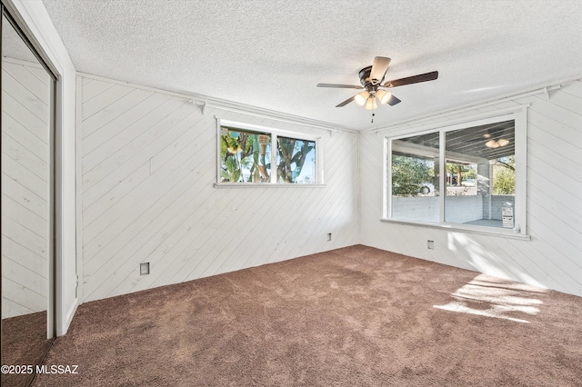 spare room featuring a ceiling fan, carpet flooring, wood walls, and a textured ceiling