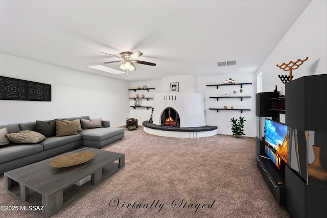 carpeted living room with a large fireplace, visible vents, and a ceiling fan