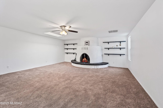 unfurnished living room featuring a ceiling fan, carpet, visible vents, and a lit fireplace