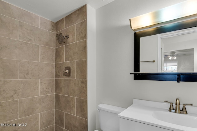 bathroom featuring a tile shower, ceiling fan, vanity, and toilet