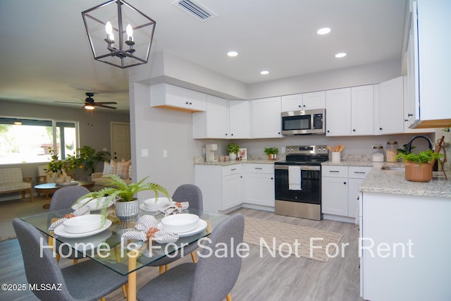 kitchen featuring appliances with stainless steel finishes, ceiling fan with notable chandelier, sink, light hardwood / wood-style flooring, and white cabinets