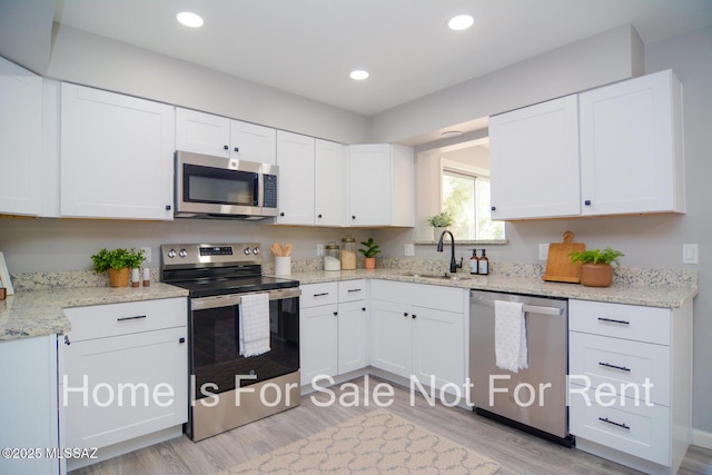 kitchen with light stone countertops, appliances with stainless steel finishes, light wood-type flooring, sink, and white cabinets