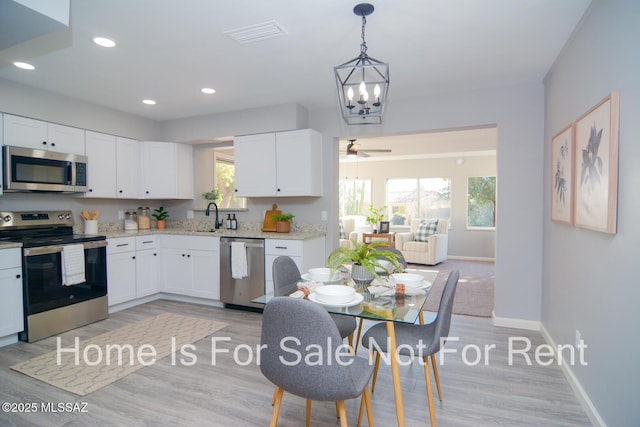 kitchen with white cabinets, decorative light fixtures, ceiling fan with notable chandelier, and stainless steel appliances