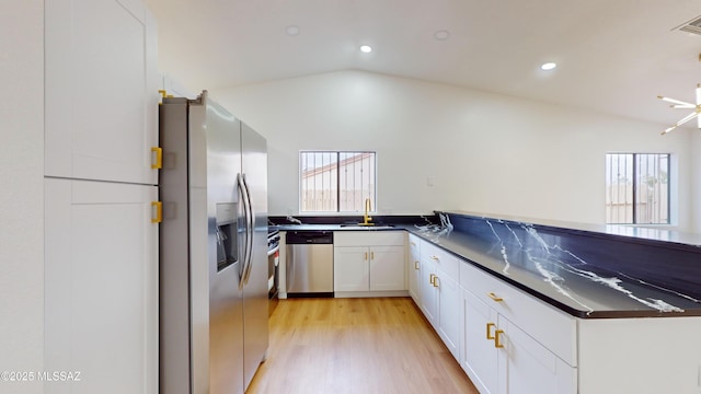 kitchen with white cabinets, stainless steel appliances, vaulted ceiling, and light hardwood / wood-style flooring