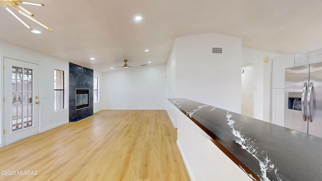 interior space featuring ceiling fan with notable chandelier, light wood-type flooring, and a high end fireplace