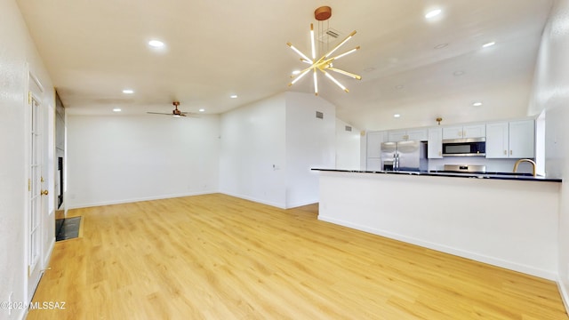 unfurnished living room featuring ceiling fan with notable chandelier, light wood-type flooring, lofted ceiling, and sink