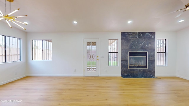 unfurnished living room featuring ceiling fan with notable chandelier, light hardwood / wood-style floors, and a fireplace