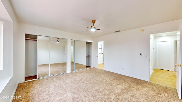 unfurnished bedroom featuring carpet flooring, ceiling fan, and multiple closets