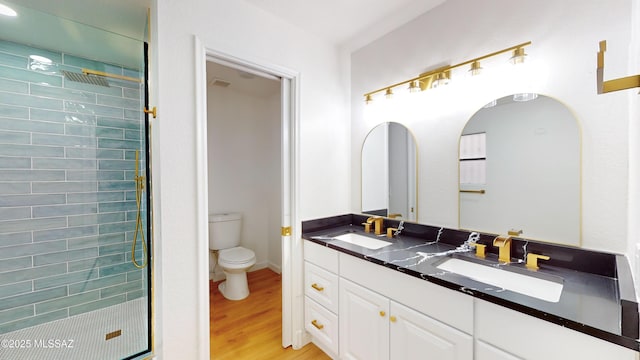 bathroom with tiled shower, vanity, wood-type flooring, and toilet