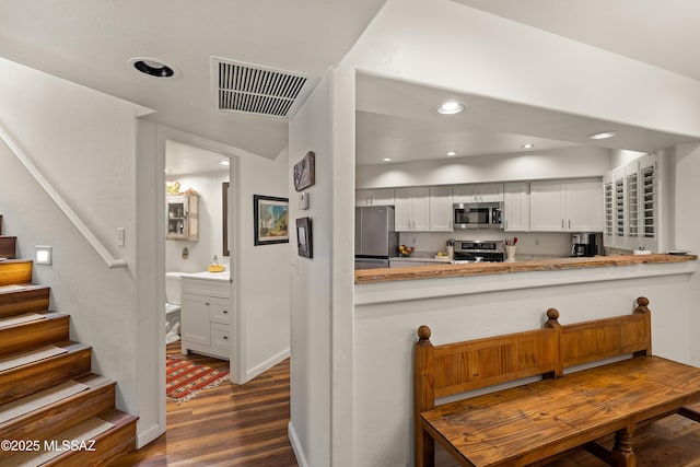 kitchen featuring dark hardwood / wood-style floors, kitchen peninsula, white cabinets, and appliances with stainless steel finishes